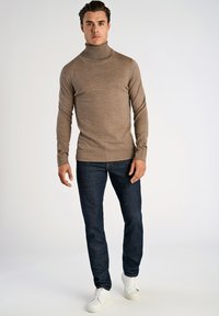 Brun polotröja med långa ärmar, kombinerad med mörkblå jeans och vita sneakers. Slät textur och figurnära design.