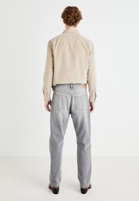Beige corduroy shirt with button cuffs, paired with light gray denim jeans featuring back pockets and a brown leather patch at the waist.