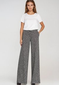 Szare i czarne spodnie o szerokich nogawkach w kratę, z wysokim stanem, dwoma bocznymi kieszeniami i zapięciem na guzik. Połączone z prostą białą koszulą z krótkim rękawem.