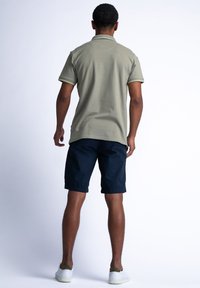 Olivgrön pikétröja med korta ärmar, kontrasterande krage, kombinerad med marinblå shorts och vita sneakers. Slät tygtextur.