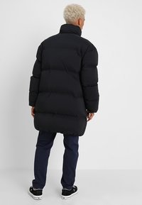 Giacca imbottita nera con collo alto, vestibilità oversize e design trapuntato. Abbinata a pantaloni blu navy e sneakers nere.