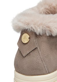 Stivale alla caviglia in suede color tan con un soffice colletto in pelliccia rosa chiaro e un accento dorato con logo circolare su una piccola toppa triangolare.