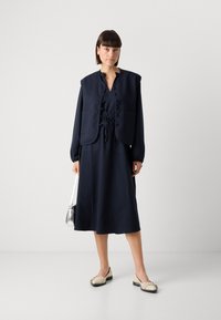 Marineblauw pinstripe jurk met een gestrikt middel, voorzien van een knoopvest en lange mouwen. Draagt het met crèmekleurige flats en een kleine zilveren tas.