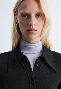 Black button-up shirt with a wide collar, layered over a light purple turtleneck. Smooth texture, no visible patterns or accents.