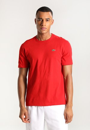 T-shirt en coton rouge avec des manches courtes, col rond et un accent logo vert sur la poitrine gauche. Texture lisse, coupe décontractée.