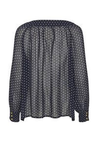 Chemisier en dentelle navy avec des pois blancs, col froncé et manches longues. Présente des poignets à boutons et un design décontracté.