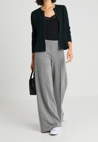 Czarna bluzka z koronką pod zielonym swetrem o teksturowym wzorze; szare szerokie spodnie z wzorem w jodełkę; białe trampki, czarna torebka.