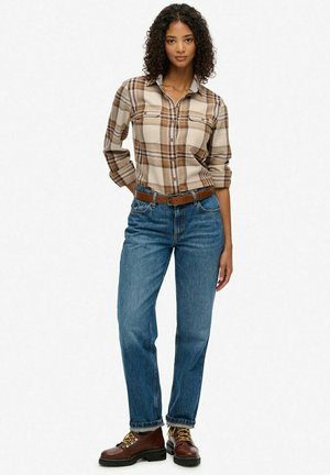 Chemise à carreaux marron et beige, jean en denim clair, ceinture marron, bottes marron avec lacets jaunes, coupe décontractée usée, tissu texturé.
