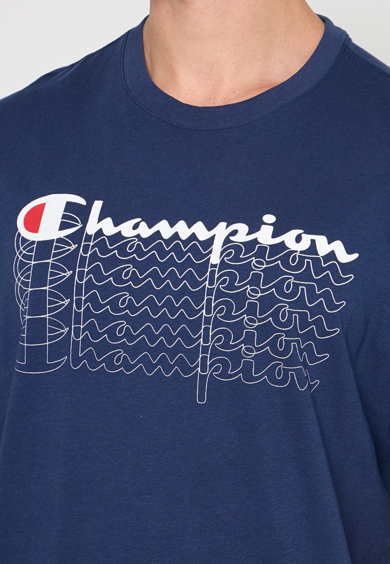 Camiseta de color azul marino hecha de algodón con un estampado gráfico blanco de la palabra "Champion" en diferentes estilos y tamaños. Cuello redondo.