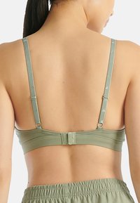 Světlá zelená sportovní podprsenka s nastavitelnými ramínky, zapínáním na há ček a oko a hladkým povrchem s minimálními detaily značky.