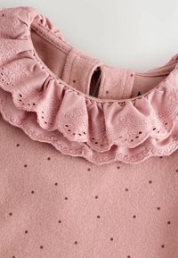 Rosa bomullstopp med en volangkrage som har dekorativ broderi och små prickar på tyget.