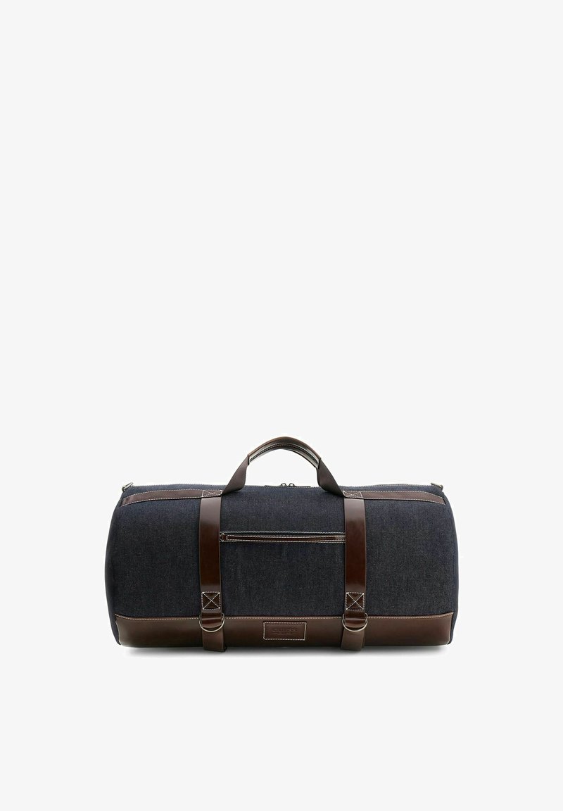 Sac de voyage bleu foncé avec des sangles en cuir marron, une poignée en cuir marron, une poche zippée à l'avant et des coutures blanches, sur fond blanc.