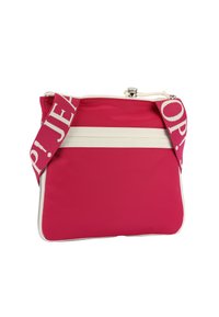 Röd nylonväska med vita vertikala ränder, med ett brett rosa band där "JEAN" är tryckt. Dragkedja på toppen och slät yta.