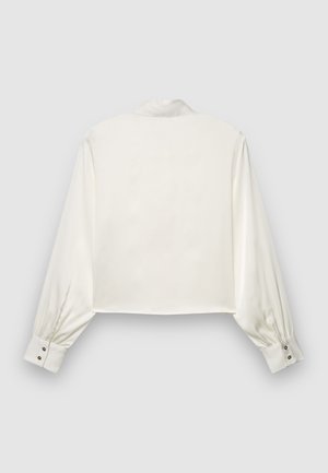 Chemise courte en satin blanc avec manches longues bouffantes et poignets boutonnés. Dotée d'un col classique et d'une texture lisse. Vue de dos présentée.