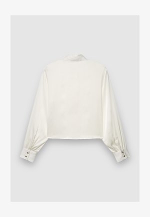 Chemise courte en satin blanc avec manches longues bouffantes et poignets boutonnés. Dotée d'un col classique et d'une texture lisse. Vue de dos présentée.