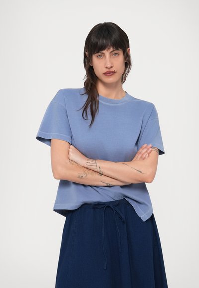 Ανεπιτήδευτο κοντομάνικο T-shirt σε ανοιχτό μπλε βαμβάκι, με στρογγυλή λαιμόκοψη και ελαφρώς χαλαρή εφαρμογή, συνδυασμένο με φούστα σε ναυτικό μπλε χρώμα με ρυθμιζόμενο κορδόνι.