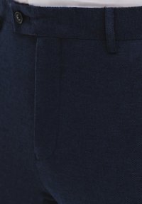 Granatowe spodnie wykonane z teksturowanej tkaniny, charakteryzujące się prostym krojem, zapięciem na guziki z przodu oraz dyskretnymi detalami kieszeni.
