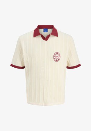 Krämfärgad kortärmad polo med en strukturerad stickad design, vinröd krage och kantning, med en röd cirkulär logotyp på bröstet.