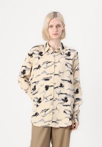 Button-up shirt in light beige with black and blue abstract floral pattern. Features a classic collar and long sleeves. Slightly loose fit.