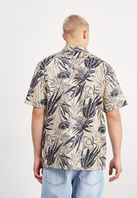 Koszula z krótkim rękawem w beżowym kolorze z granatowym wzorem kwiatowym, z kołnierzykiem i luźnym krojem. Wykonana z lekkiej tkaniny o gładkiej fakturze.