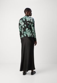 Langarmtop met zwarte basis en groene bloemenprint; gecombineerd met een lange zwarte rok; gladde stof, slanke pasvorm, subtiele glans.