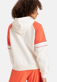 Hooded sweatshirt in cream and coral, featuring contrasting sleeves, ribbed cuffs, and a red accent stripe on the shoulders. Soft texture.