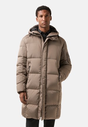 Beige pufferjack met een capuchon, voorzien van een gewatteerd ontwerp, met ritszakken aan de zijkant en een relaxte pasvorm, gemaakt van waterafstotend materiaal.