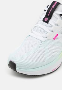 Baskets bleu clair et blanches avec un dessus en maille texturée, accents noirs et roses sur la languette, et une semelle en caoutchouc au design dégradé.