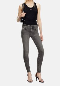 Svart linne med en logotyp, kombinerat med åtsittande grå skinny jeans och svarta klacksandaler, som visar en stilren design och minimalistisk stil.