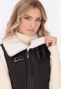 Zwart en crèmekleurig vest met een faux shearling kraag, ritssluiting en metalen hardware accenten met verstelbare gespen en drukknoopdetails.