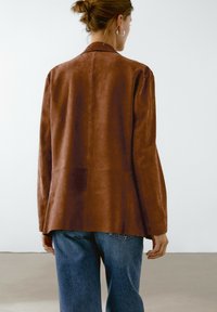 Brun mocka blazer med skräddarsydd passform, med klassisk krage och långa ärmar, ihop med lösa blå denimjeans.