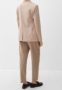Blazer beige a righe sottili con taglio sartoriale, abbinato a pantaloni beige. Mocassini neri completano l'outfit. Linee pulite e design minimale.