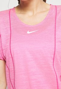 Mujer vistiendo una camiseta deportiva rosa de Nike con mangas cortas y un logotipo blanco de Nike centrado debajo del escote.