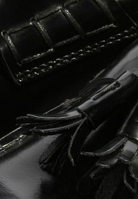 Crne lakirane cipele s elegantnim dizajnom, dekorativnim resicama i detaljima šivanja; glatka tekstura s sjajnim završetkom.