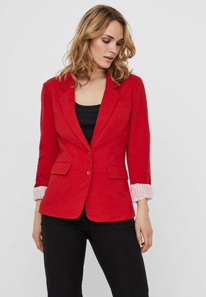 Červený blazer s přiléhavým střihem, jedním knoflíkovým zapínáním, dvěma předními kapsami a pruhovanými akcenty na manžetách. Nositelný přes černý top.