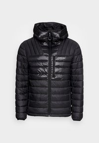 Zwarte gewatteerde jas met een hoge kraag, doorgestikte textuur, ritssluiting aan de voorkant en een borstzak. Heeft een Calvin Klein-logo aan de linkerkant.