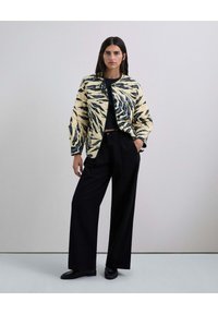 Chaqueta acolchada estampada con base crema y rayas de tigre en negro y azul, combinada con pantalones anchos negros y zapatos negros.