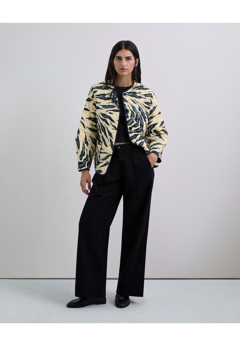 Chaqueta acolchada estampada con base crema y rayas de tigre en negro y azul, combinada con pantalones anchos negros y zapatos negros.