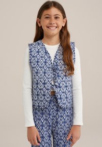 Sininen ja valkoinen kuvioitu liivi, jossa on solkikiinnitys, seuranaan pitkähihaisia valkoisia paitoja ja vastaavat kuviolliset housut. Sileä kankaan rakenne.