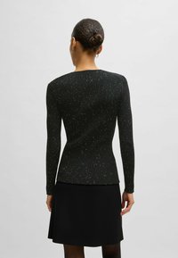Svart ribbad tröja med långa ärmar, prydd med silverprickar. Designen har en figurnära silhuett och en rund halsringning.