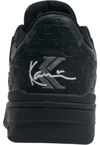Fekete sneakers dombornyomott mintával, fehér aláírással és logóval a saroknál. A talp lapos és texturált.