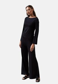 Czarny komplet z długim rękawem i szerokimi spodniami, wykonany z miękkiego materiału; charakteryzuje się luźnym krojem o minimalistycznym designie i gładkiej teksturze.