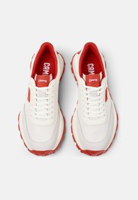 Sneakers bianchi con accenti rossi, tomaia in tessuto testurizzato, zeppa bianca spessa e suola rossa resistente. Presentano lacci e branding Camper.