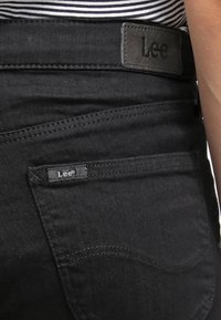 I jeans in denim nero presentano una tasca posteriore visibile con un piccolo etichetta Lee, completata da un'etichetta in pelle testurizzata sulla cintura.