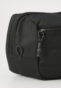 Black textured fabric pouch with front zipper pocket and loop pull cords on a neutral background.