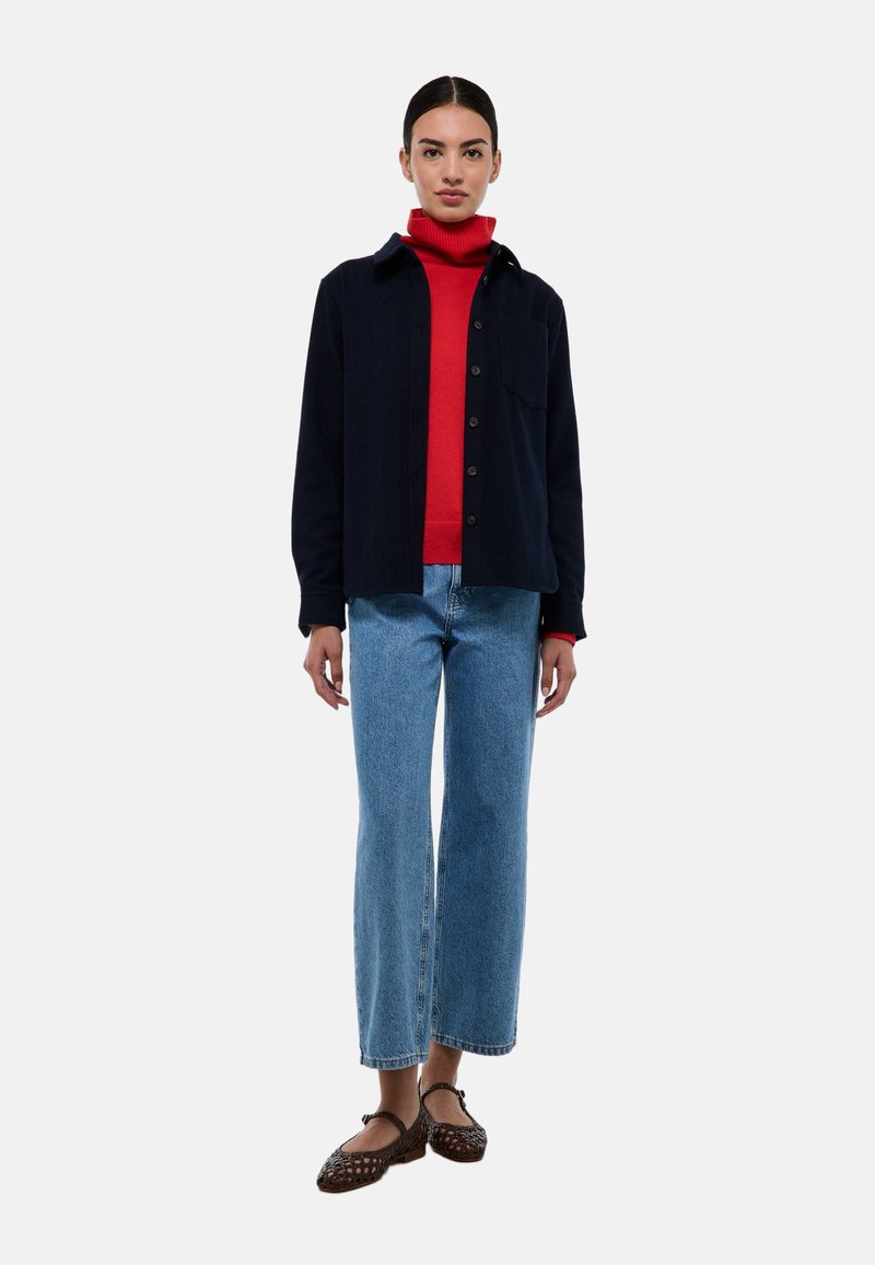Chemise bleu marine à boutons sur un turtleneck rouge, associée à un jean taille haute bleu et des ballerines tressées marron. Design simple et coupe décontractée.