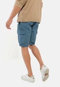 Blå cargo shorts med sidelommer, fremstillet af letvægtsstof. Samlet med hvide sneakers med grå detaljer og strukturerede såler.