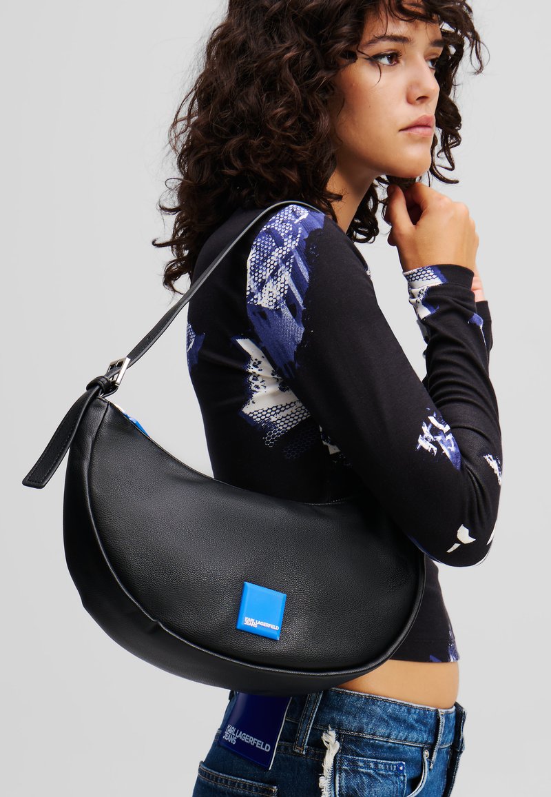 Black leather shoulder bag with a curved shape, featuring a blue brand logo and a short strap. Smooth texture and minimalist design.