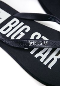 Juodai šlepetės su tekstūruotu dirželiu, kurių pado centre yra iškilus baltas „BIG STAR“ logotipas, pagamintos iš minkštos medžiagos.