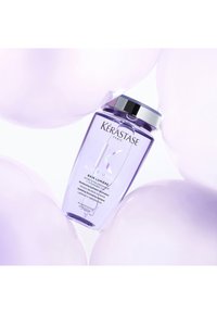 Flacon de shampooing hydratant Kérastase Blond Absolu Bain Lumière entouré de ballons violets doux sur fond blanc.